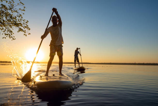 Two people stand-up paddleboarding on a calm lake at sunset